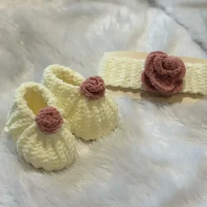 Handmade crochet Product : cream colorerd baby booties paired with a matching crochet headband, each adorned with a soft dusty-rose flower, displayed on a fluffy white background for a cozy, premium look.