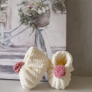 Handmade crochet baby booties in soft cream color with pink crochet flower detail, cozy crochet footwear for newborns and infants.